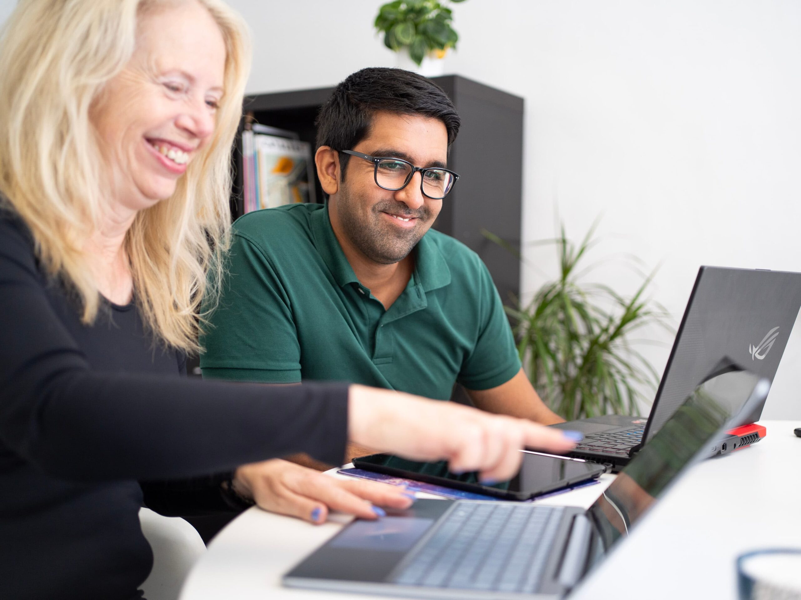 A man and a woman pointing towards a laptop smiling
